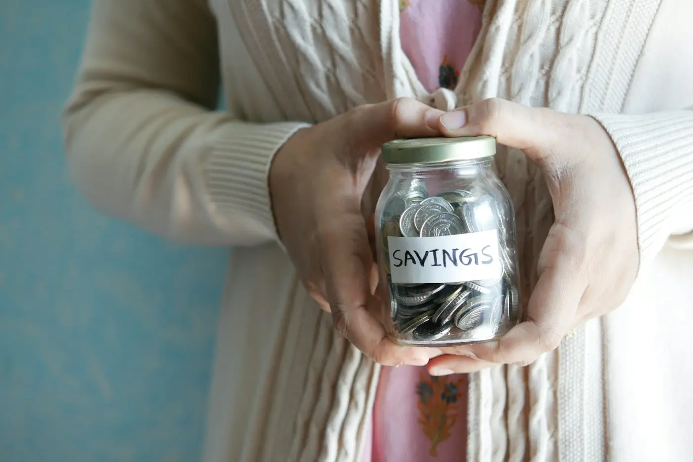 Hands holding a glass jar of coins labeled Savings