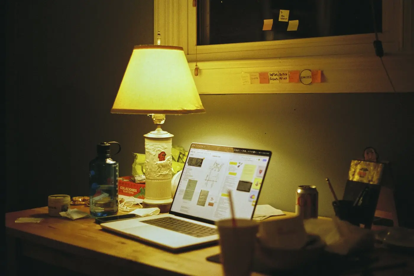 A laptop open on a desk under a warm lamp in the evening
