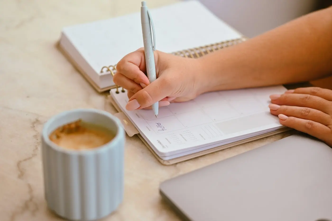 A person writing in a planner next to a coffee mug