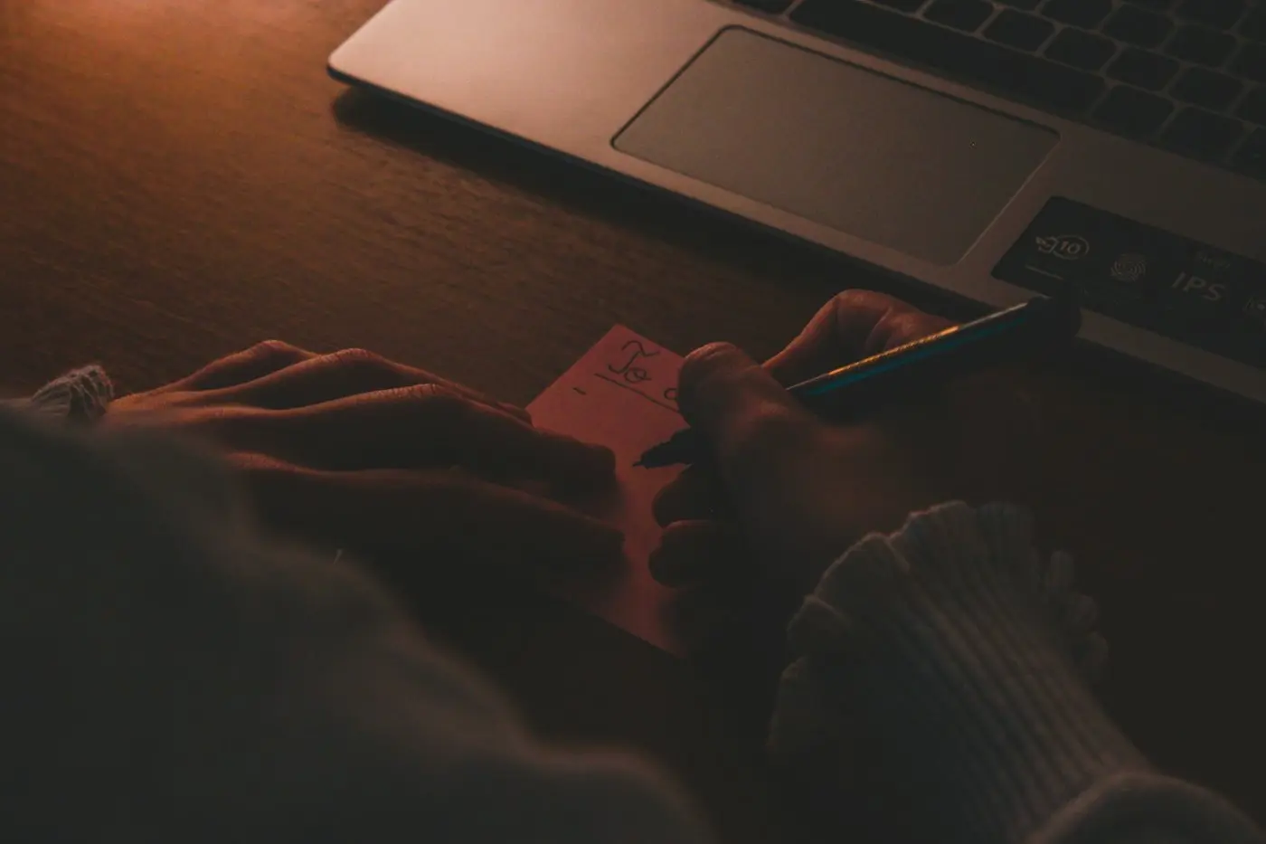 Hands writing a note beside a laptop in warm evening light