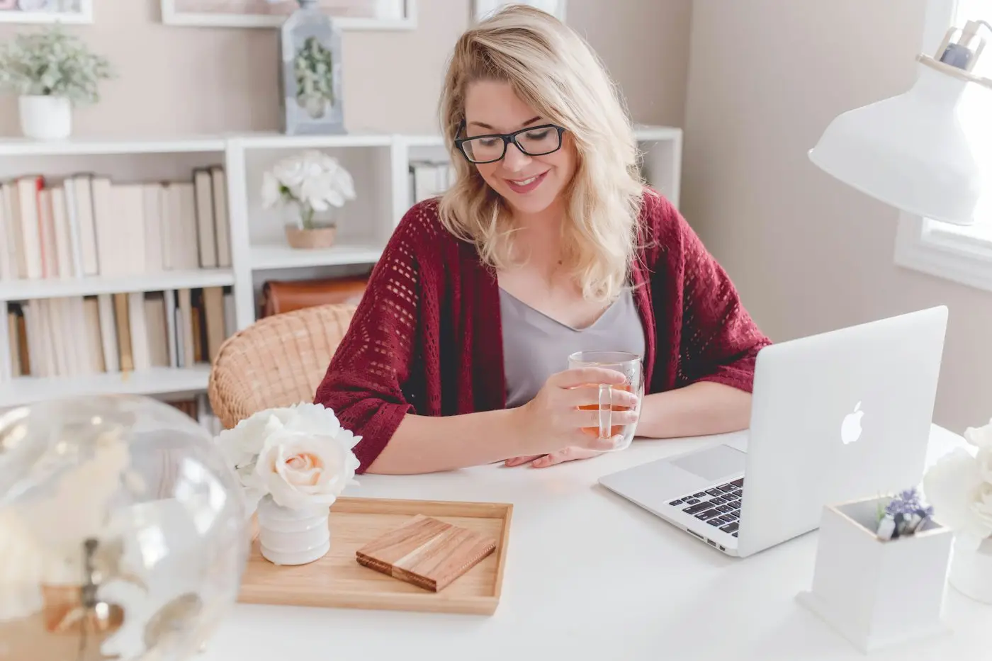 A woman smiling with a coffee mug beside her laptop